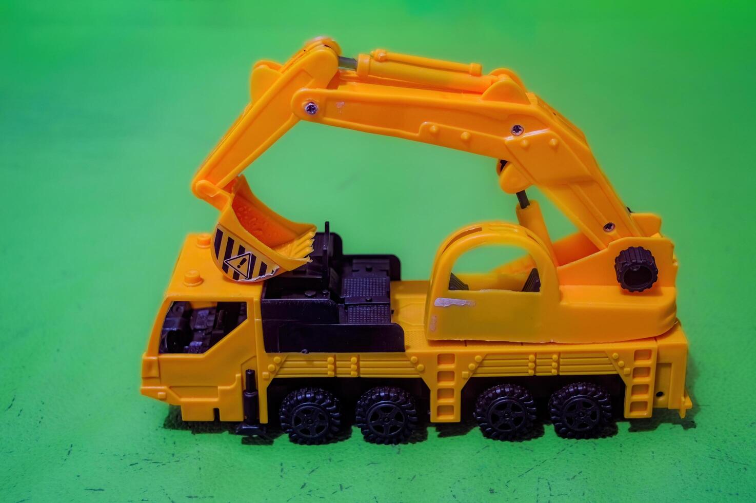 a yellow toy miniature excavator on a flat green background photo