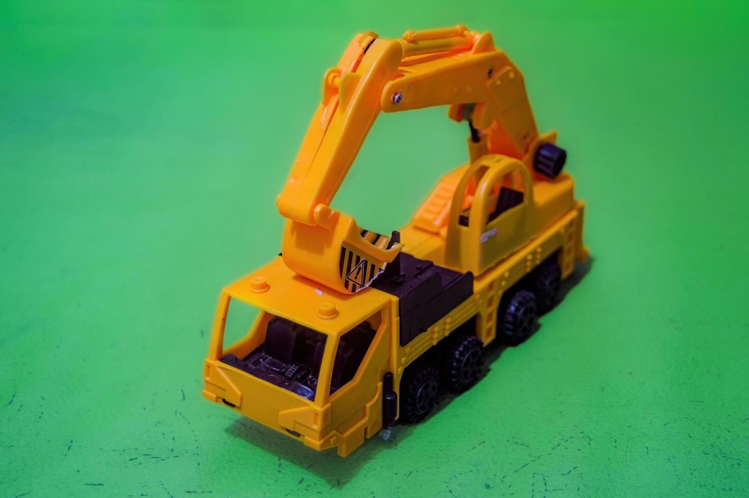 a yellow toy miniature excavator on a flat green background photo