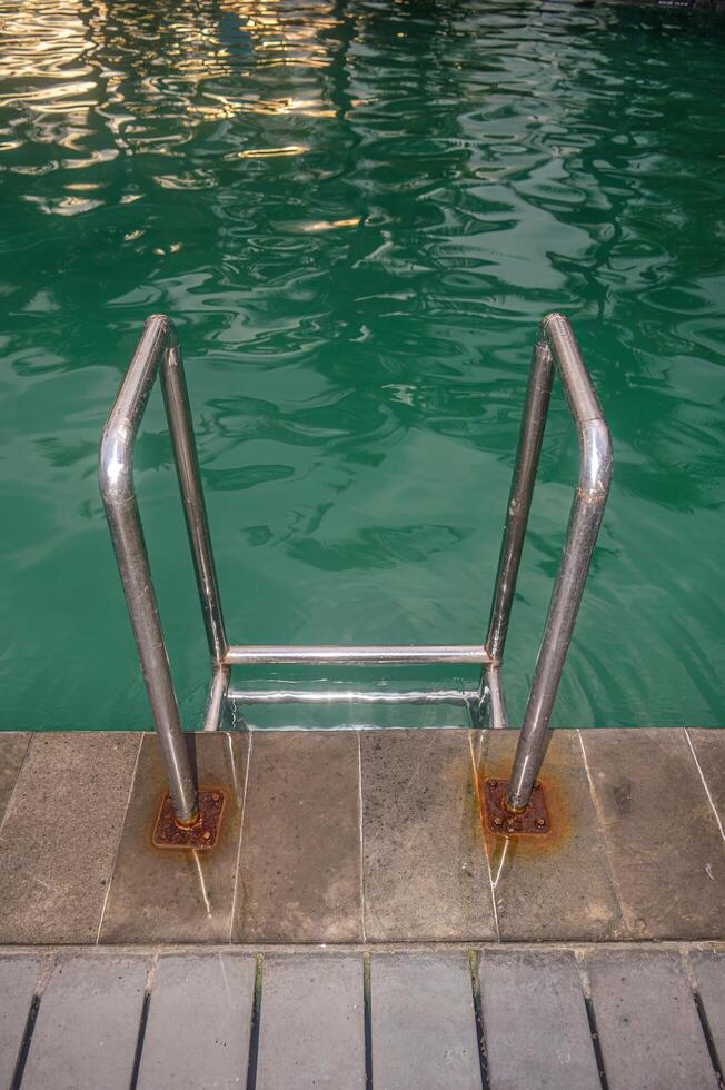 a stainless steel swimming ladder in a swimming pool with turquoise water photo