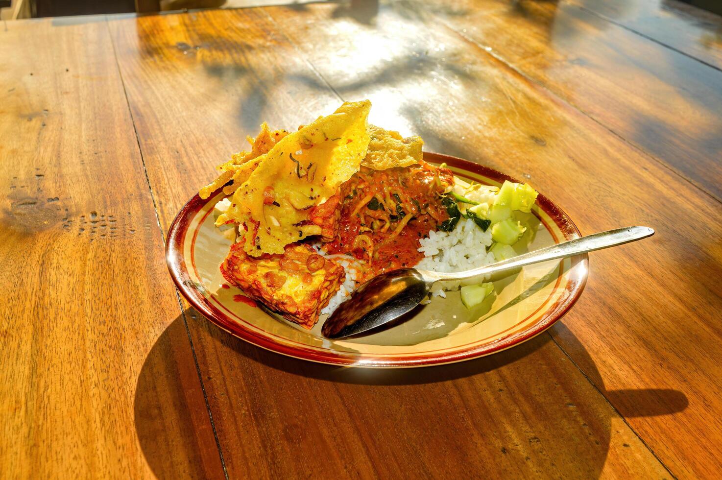 a plate of East Javanese Madiun pecel rice on a wooden table in the morning sunlight photo