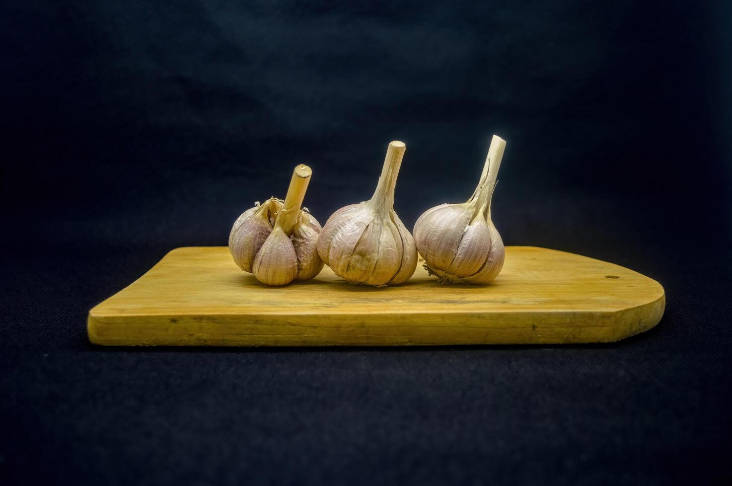 three garlic cloves arranged on a cutting board isolated on black background photo