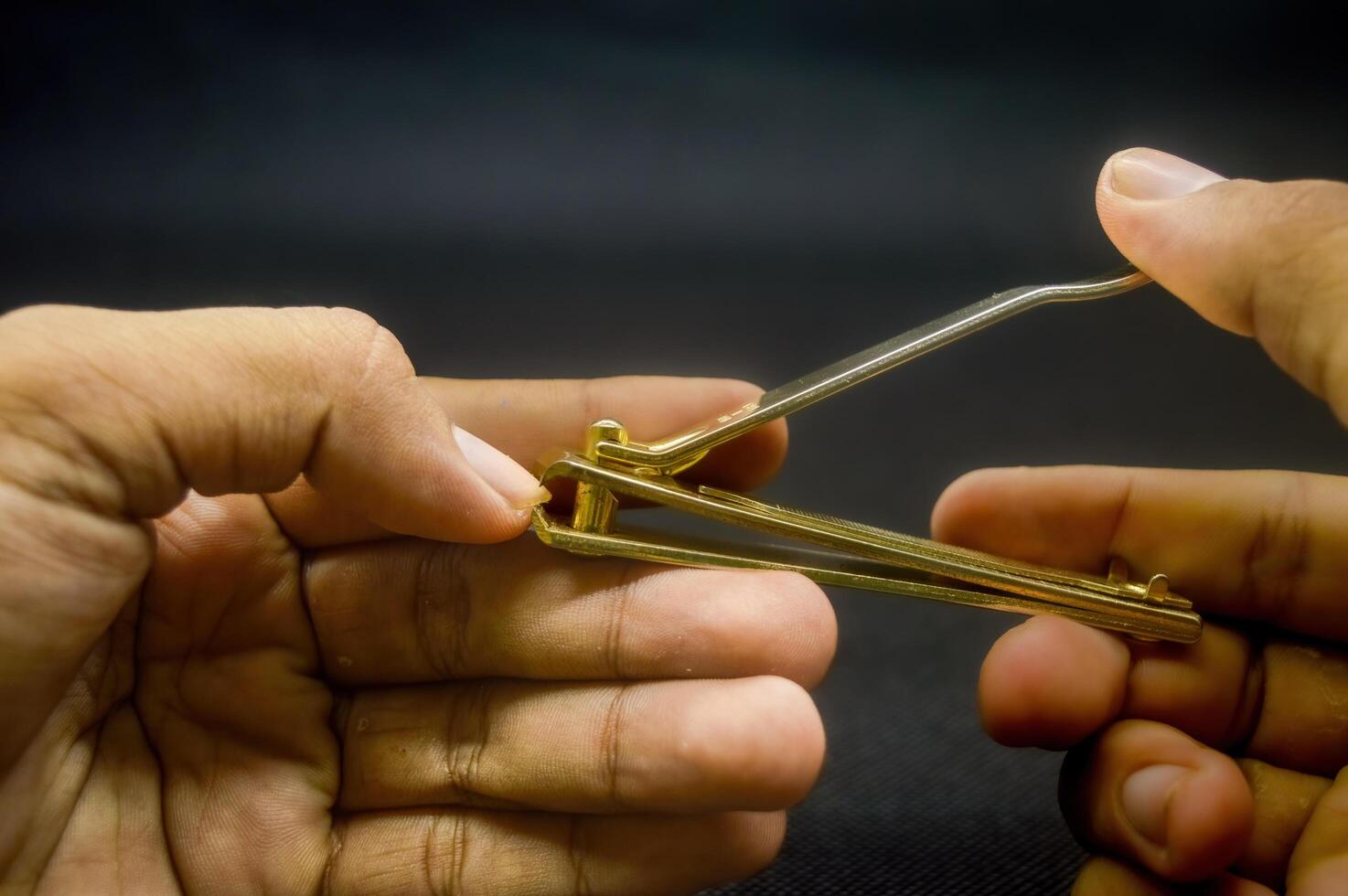 hand cutting nails using a gold nail clipper isolated on black background photo