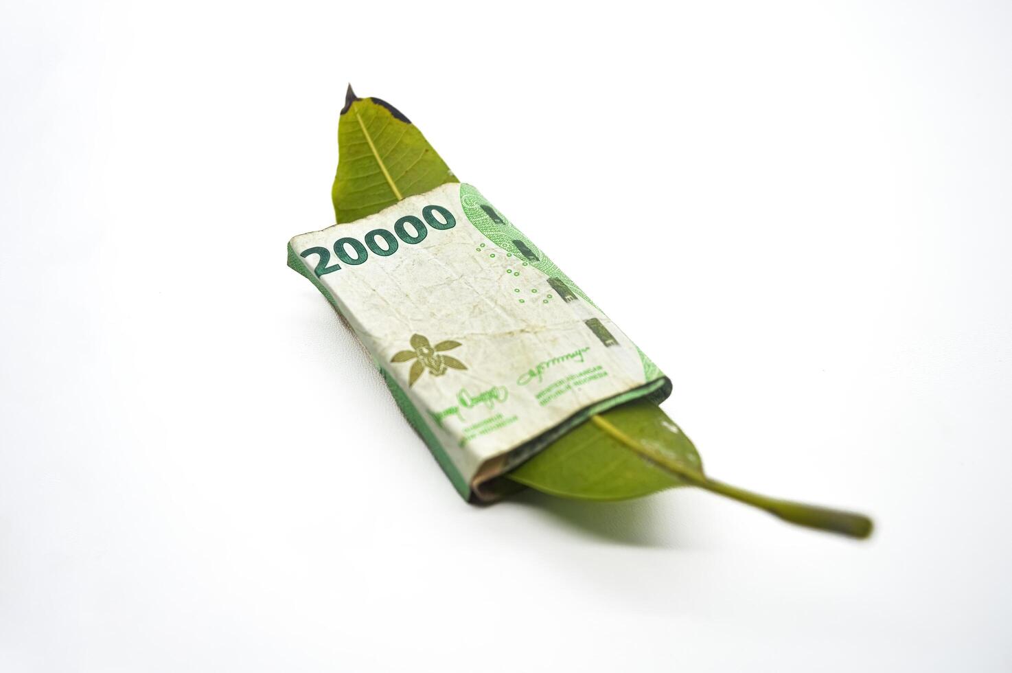 leaf wrapped in money worth twenty thousand rupiah isolated on white background photo