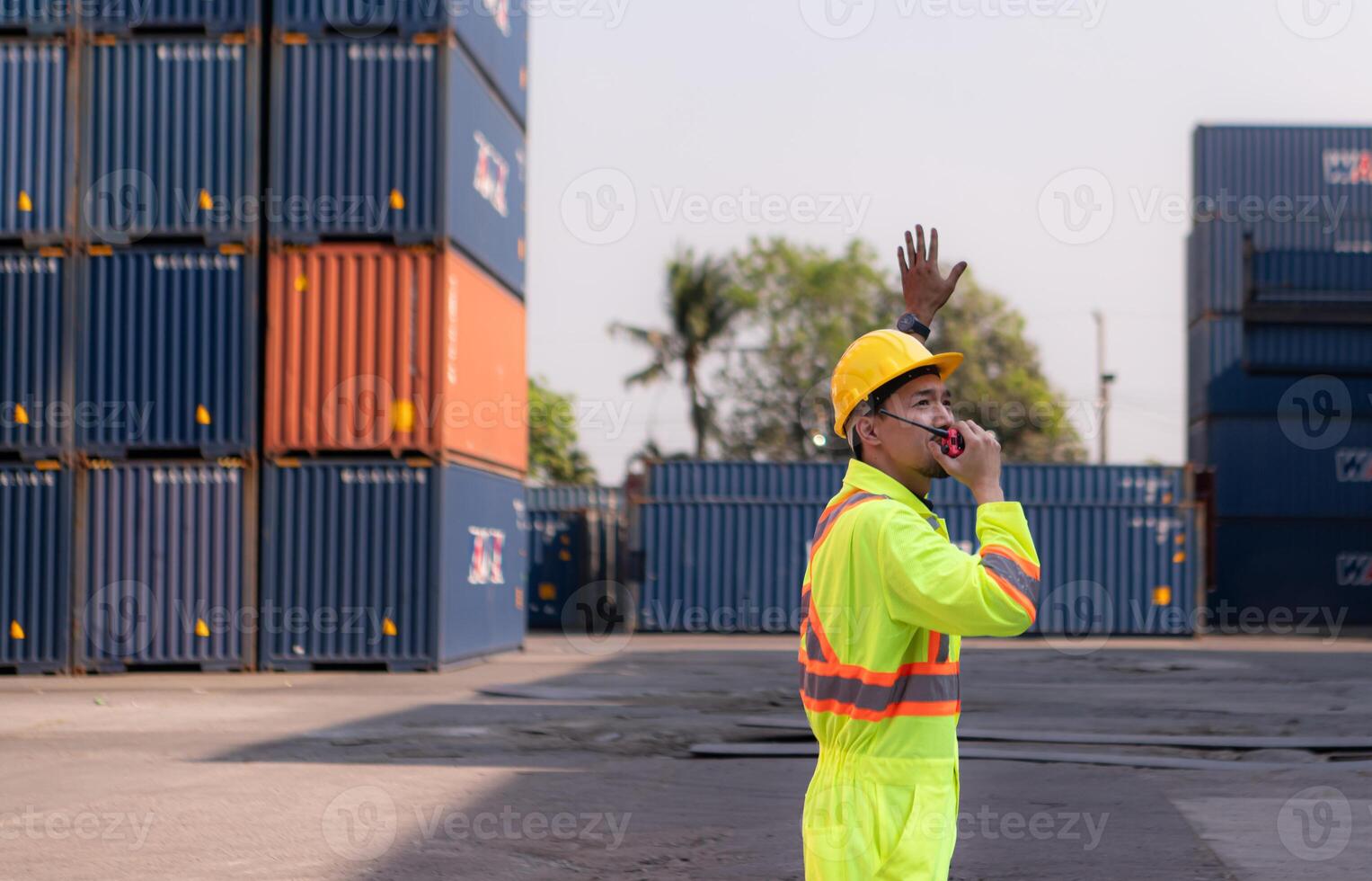Workers in the import and export industry use walkie talkies to communicate with drivers of reach stacker containers in an empty container warehouse. photo