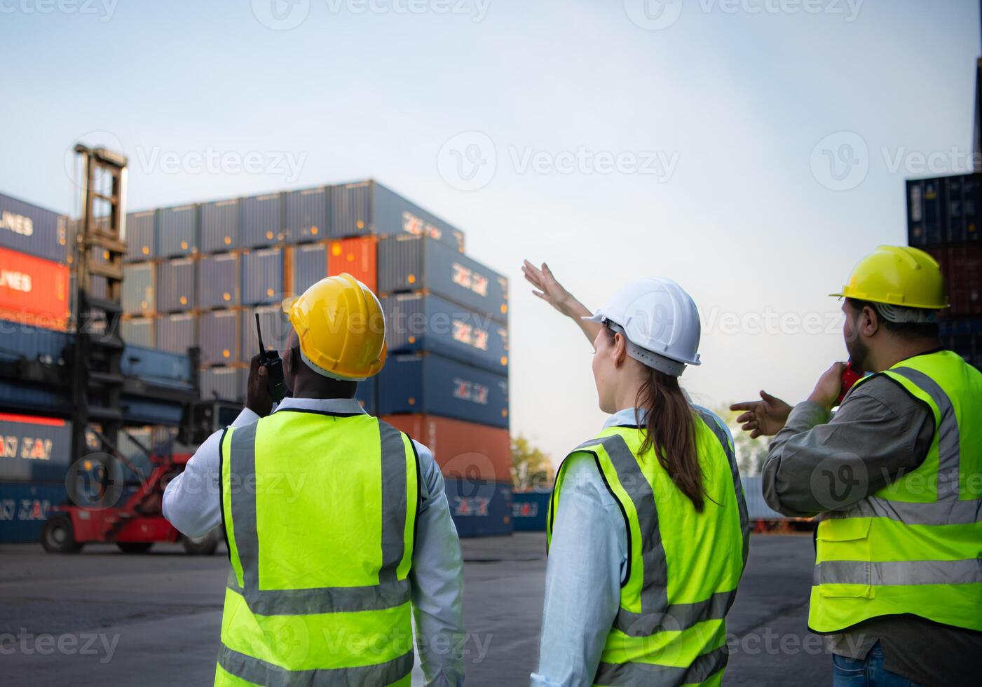 Group of workers in the import and export industry use walkie talkies to communicate with drivers of reach stacker containers in an empty container warehouse. photo