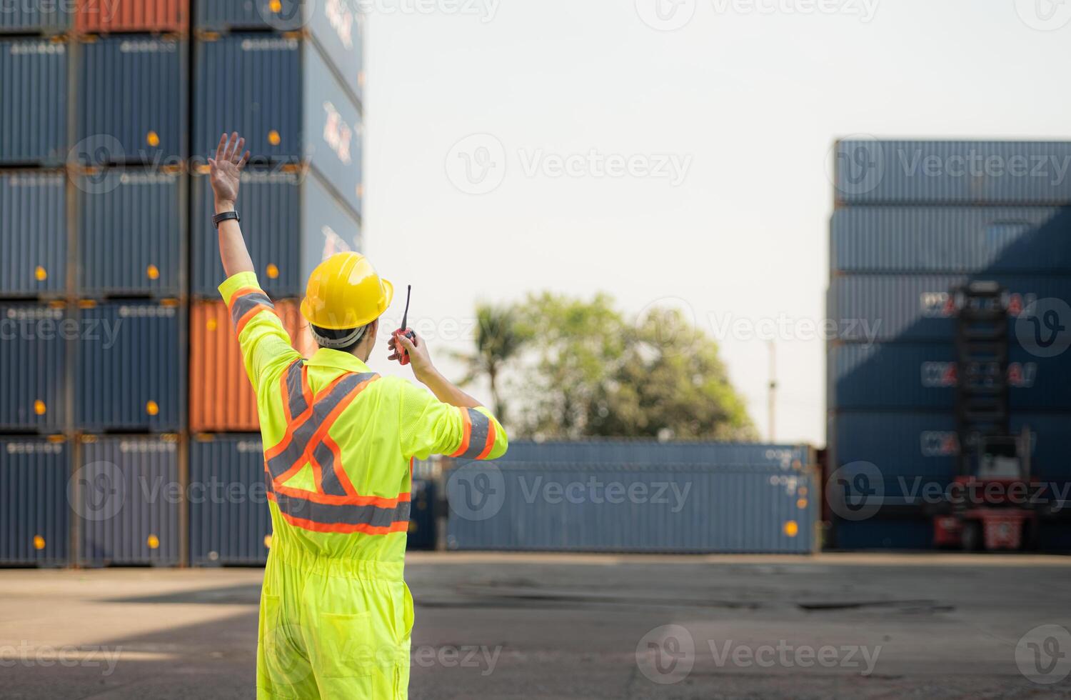 Workers in the import and export industry use walkie talkies to communicate with drivers of reach stacker containers in an empty container warehouse. photo