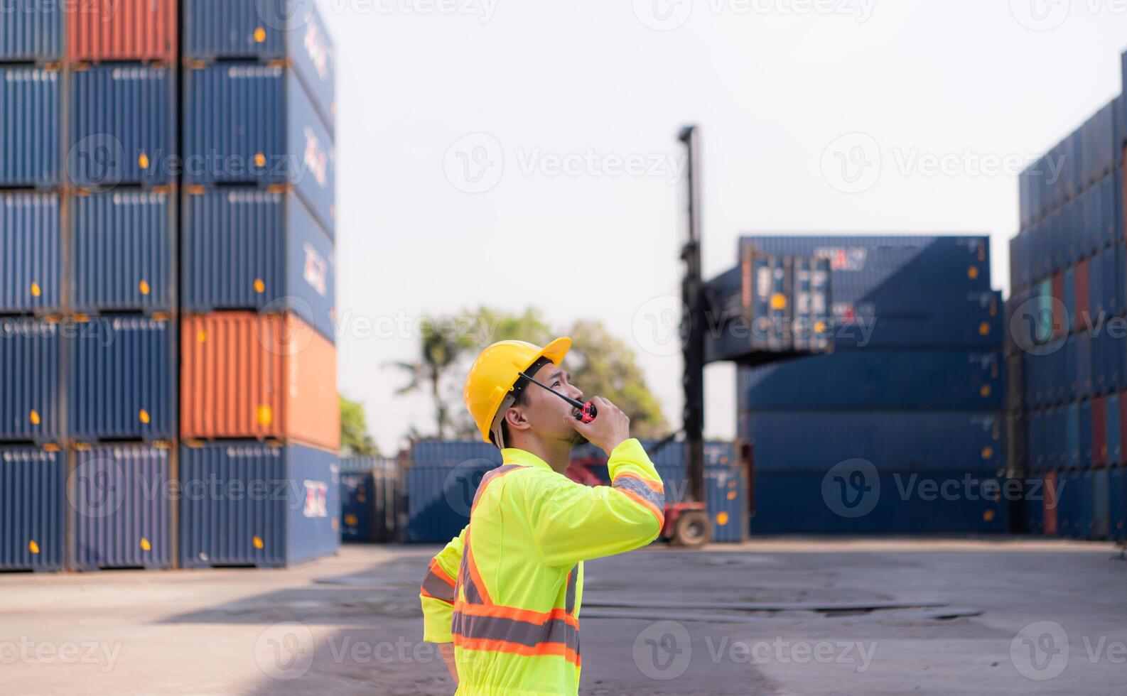 Workers in the import and export industry use walkie talkies to communicate with drivers of reach stacker containers in an empty container warehouse. photo