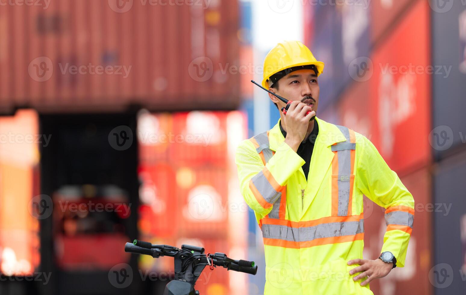 Portrait of a warehouse worker speaking on a walkie talkie with a coworker in an empty container warehouse while driving a scooter to inspect work photo