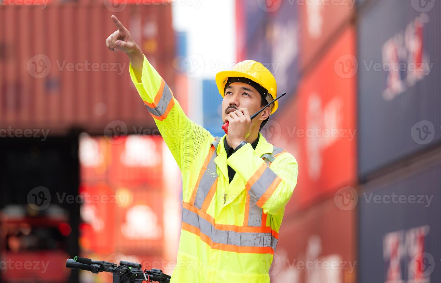 Portrait of a warehouse worker speaking on a walkie talkie with a coworker in an empty container warehouse while driving a scooter to inspect work photo