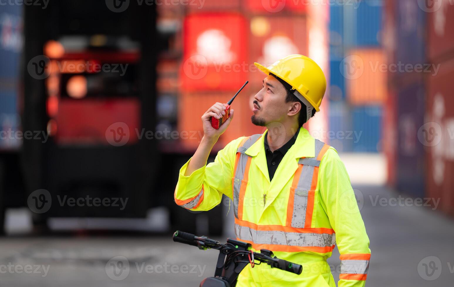 Portrait of a warehouse worker speaking on a walkie talkie with a coworker in an empty container warehouse while driving a scooter to inspect work photo