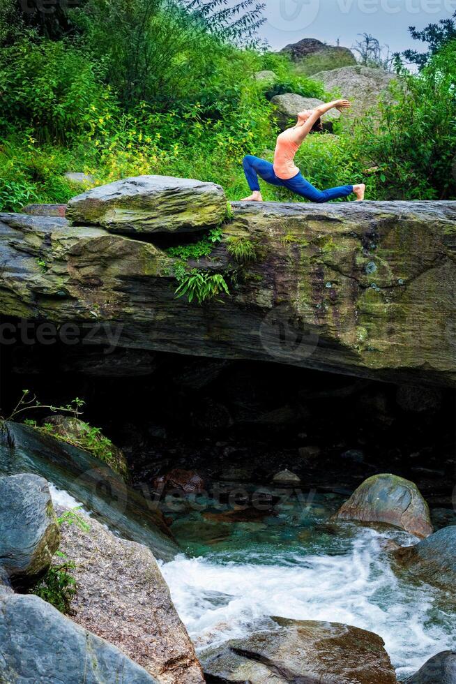 Sporty fit woman practices yoga Anjaneyasana in mountains photo