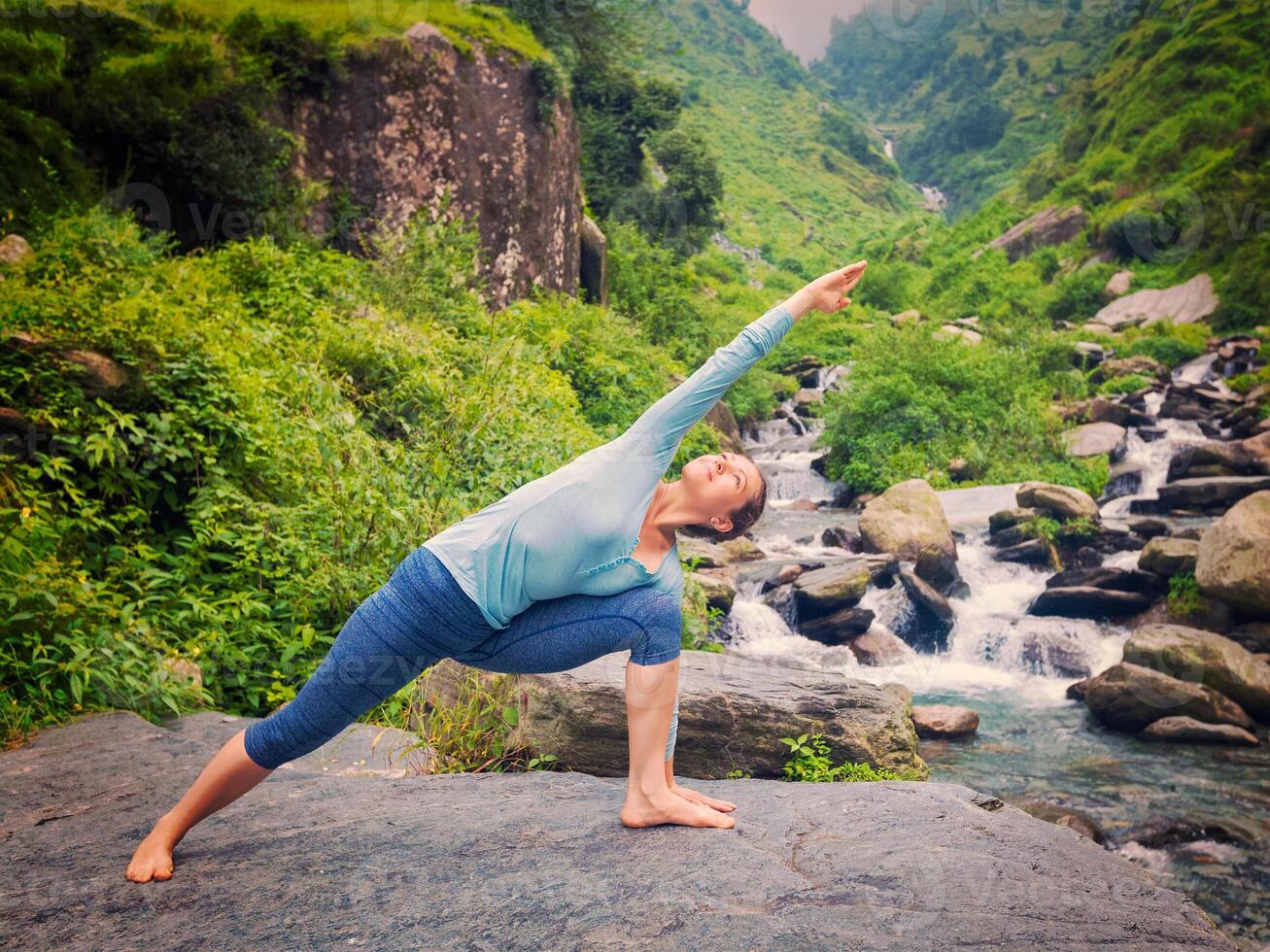 Woman practices yoga asana Utthita Parsvakonasana outdoors photo