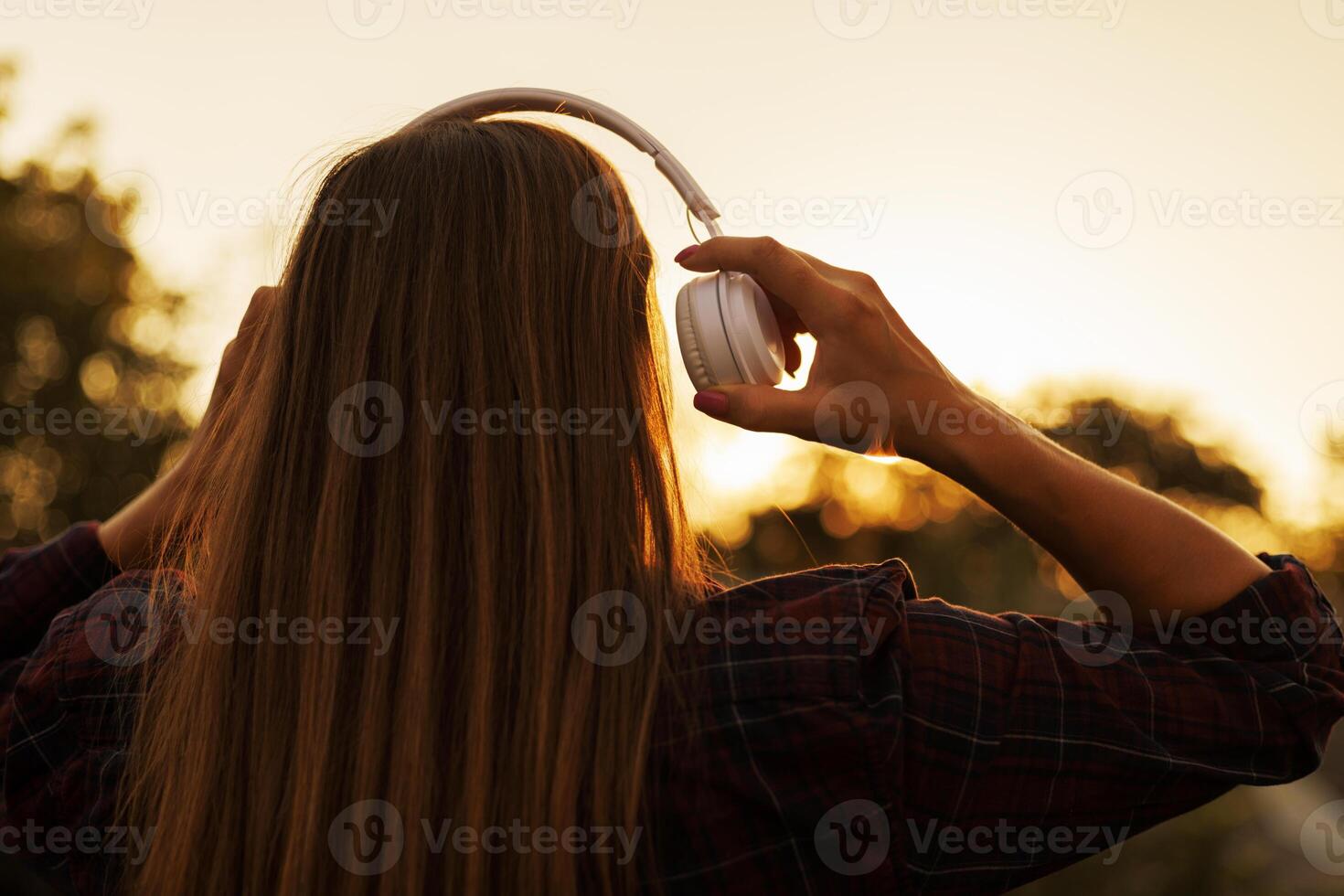 Young woman in headphones listening to music at sunset photo