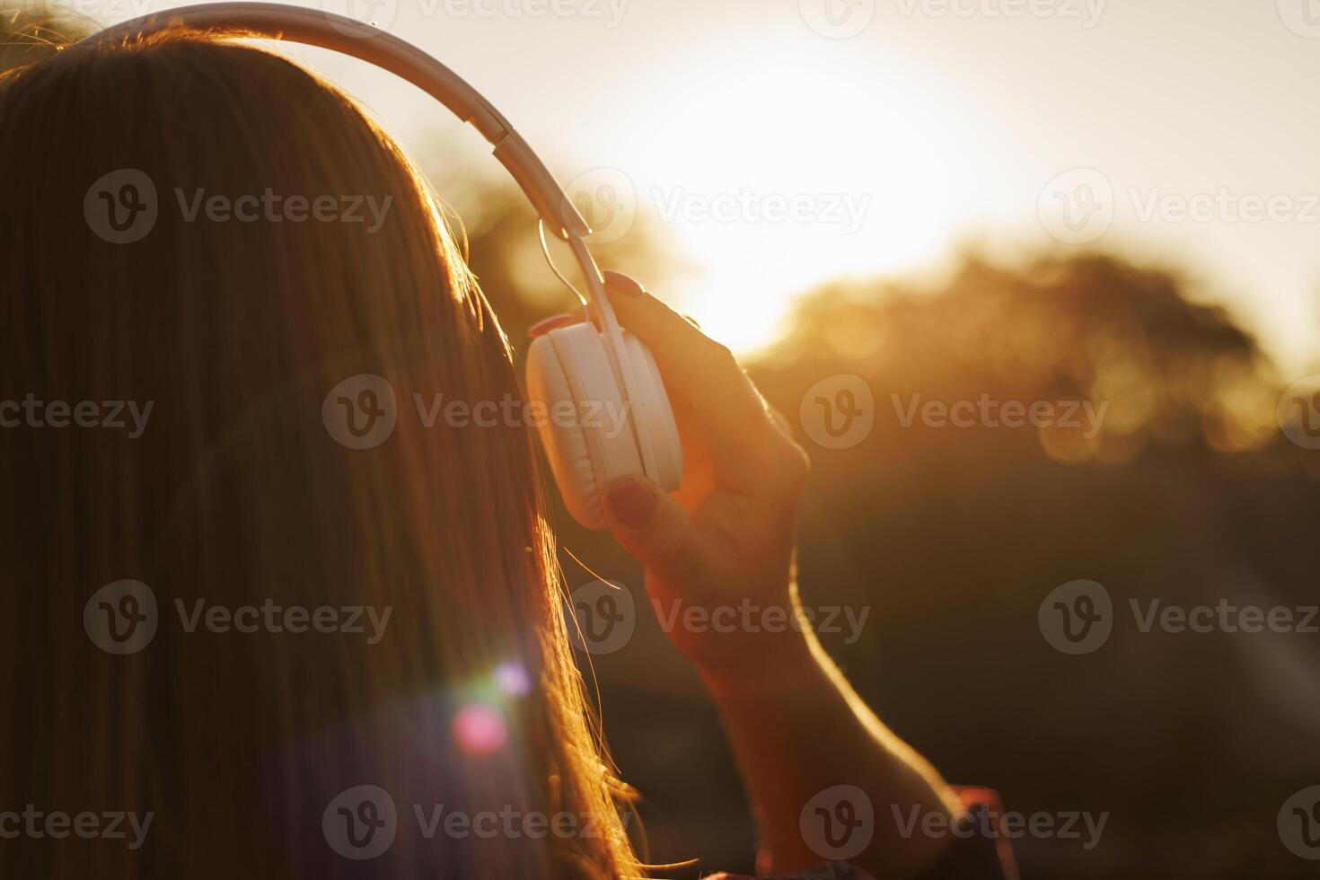 Young woman in headphones listening to music at sunset photo