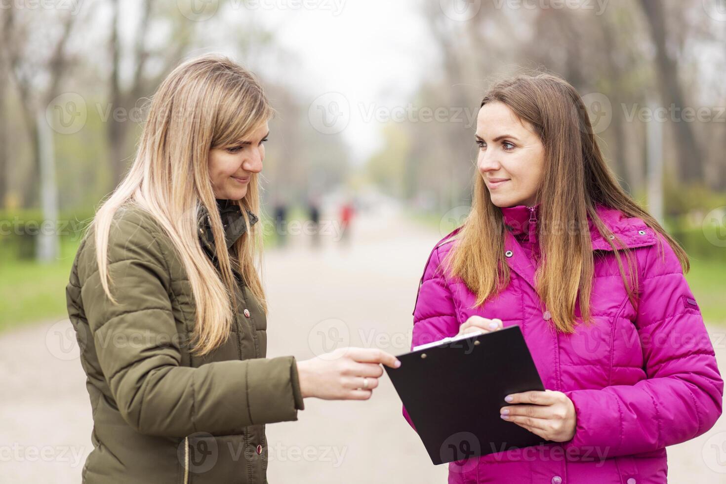 Two women engaged in a conversation with a clipboard on a park path photo