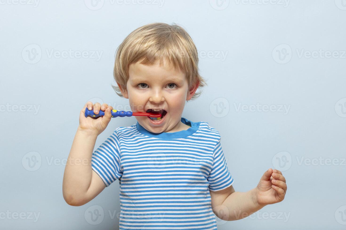 Little blonde boy brushing teeth with toothbrush on blue background photo