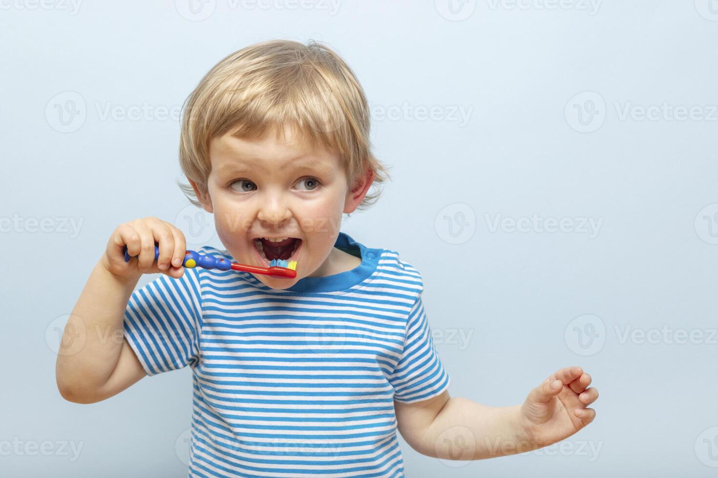 Little blonde boy brushing teeth with toothbrush on blue background photo