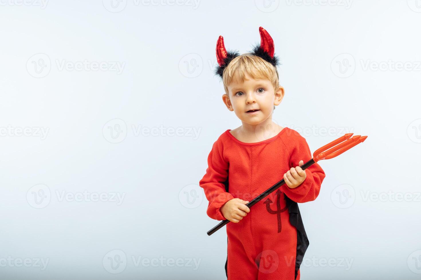 Happy cheerful boy in devil costume with trident on blue background photo
