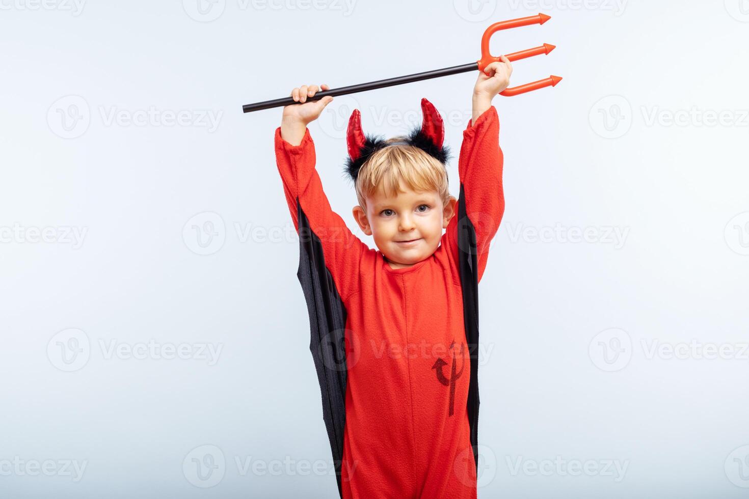 Happy cheerful boy in devil costume with trident on blue background photo