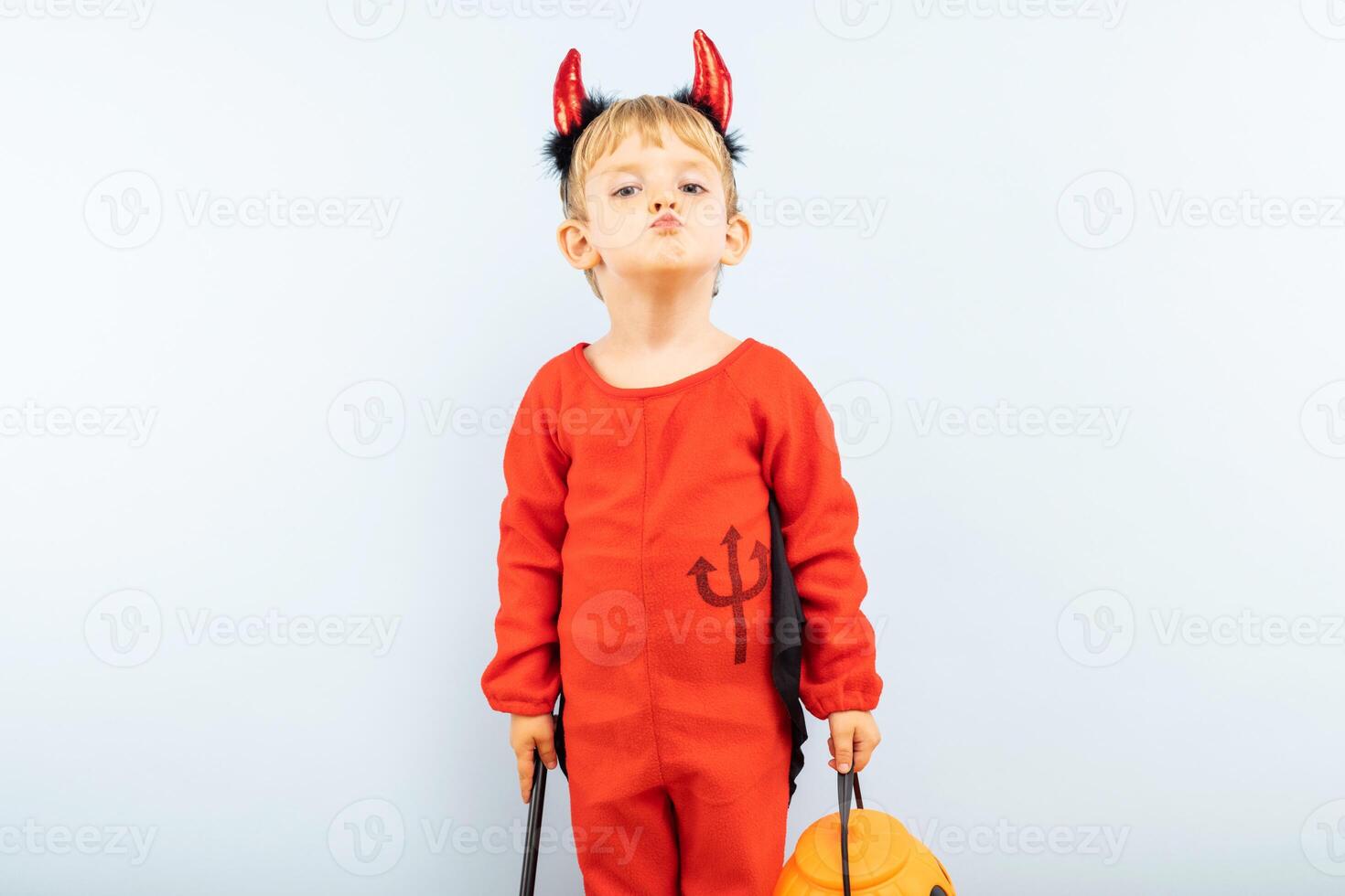Happy cheerful boy in devil costume with trident on blue background photo