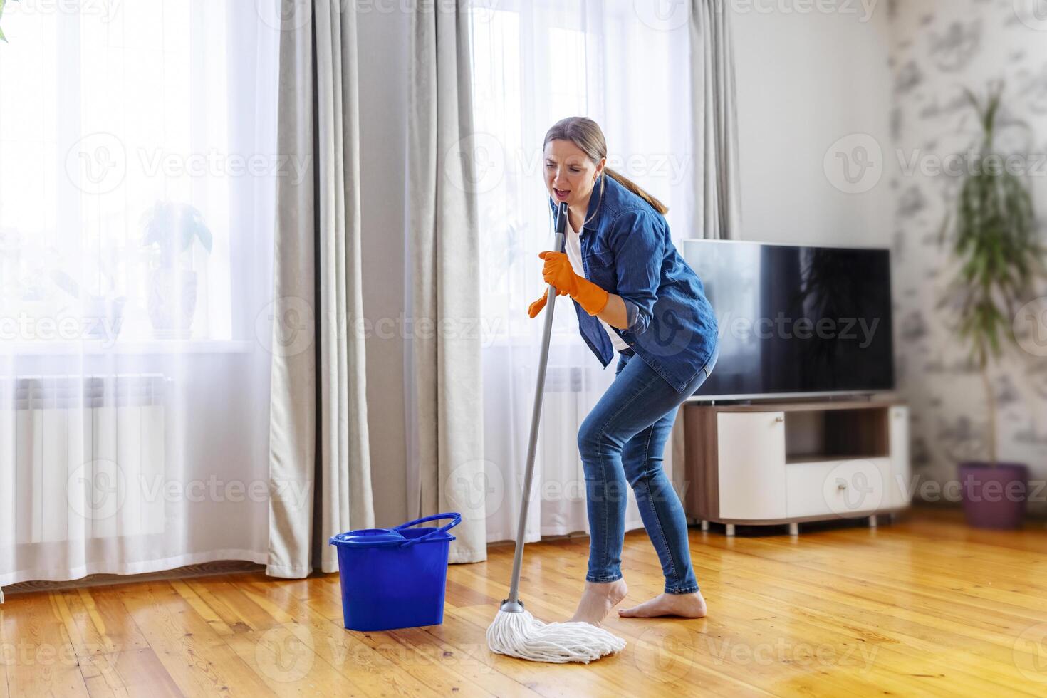 contento joven mujer con fregona cantando, bailando y teniendo divertido mientras limpieza piso foto