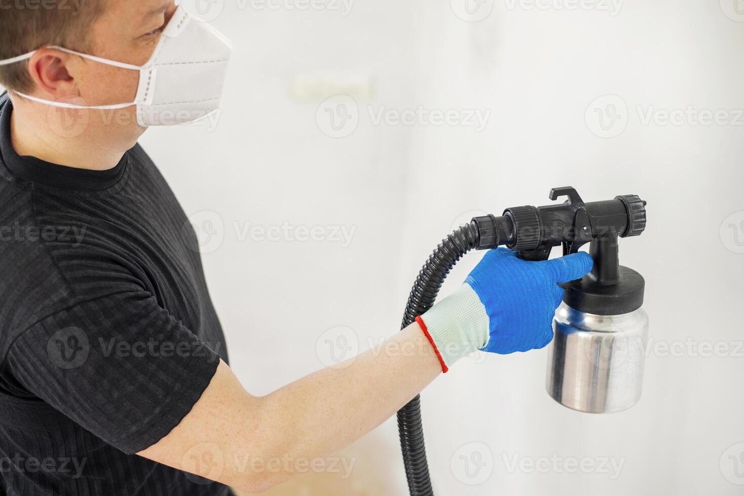 Worker in protective mask painting wall with spray gun photo