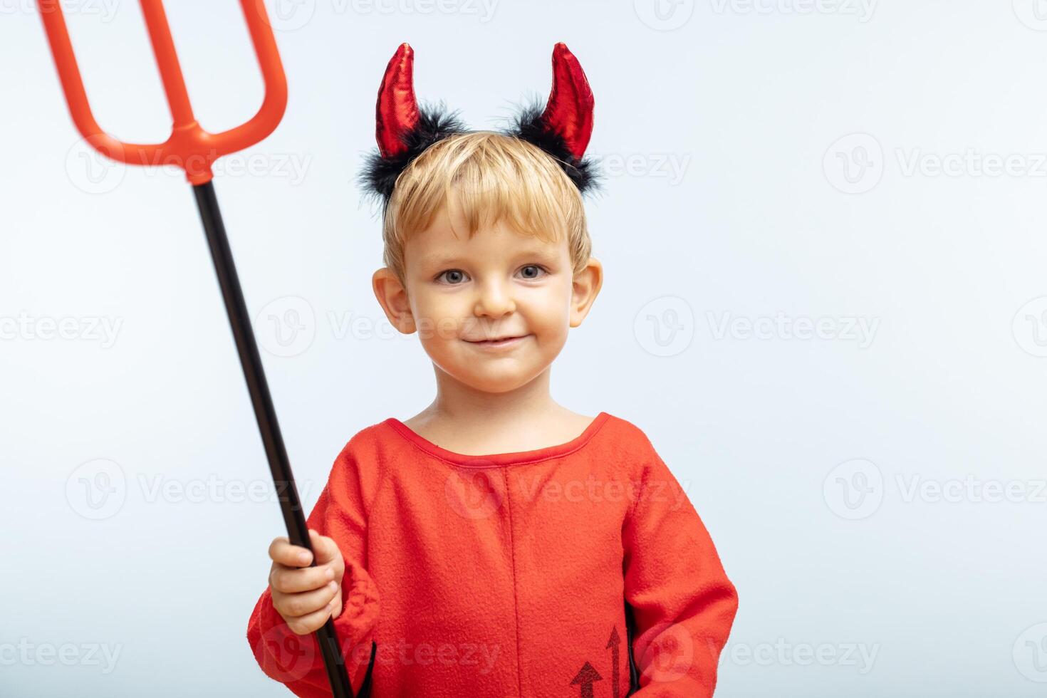 Happy cheerful boy in devil costume with trident on blue background photo