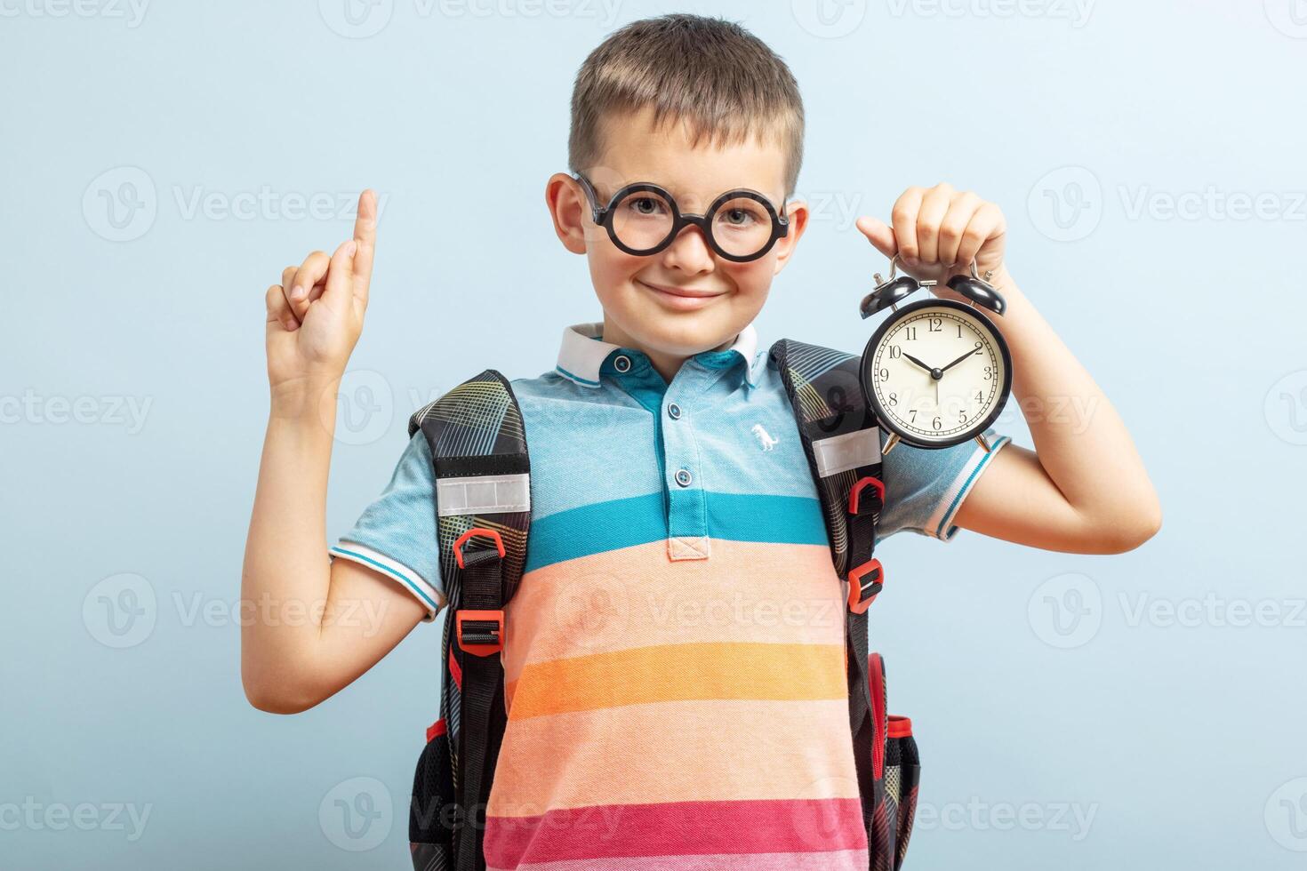 A cute school boy in glasses with an alarm clock against blue background photo