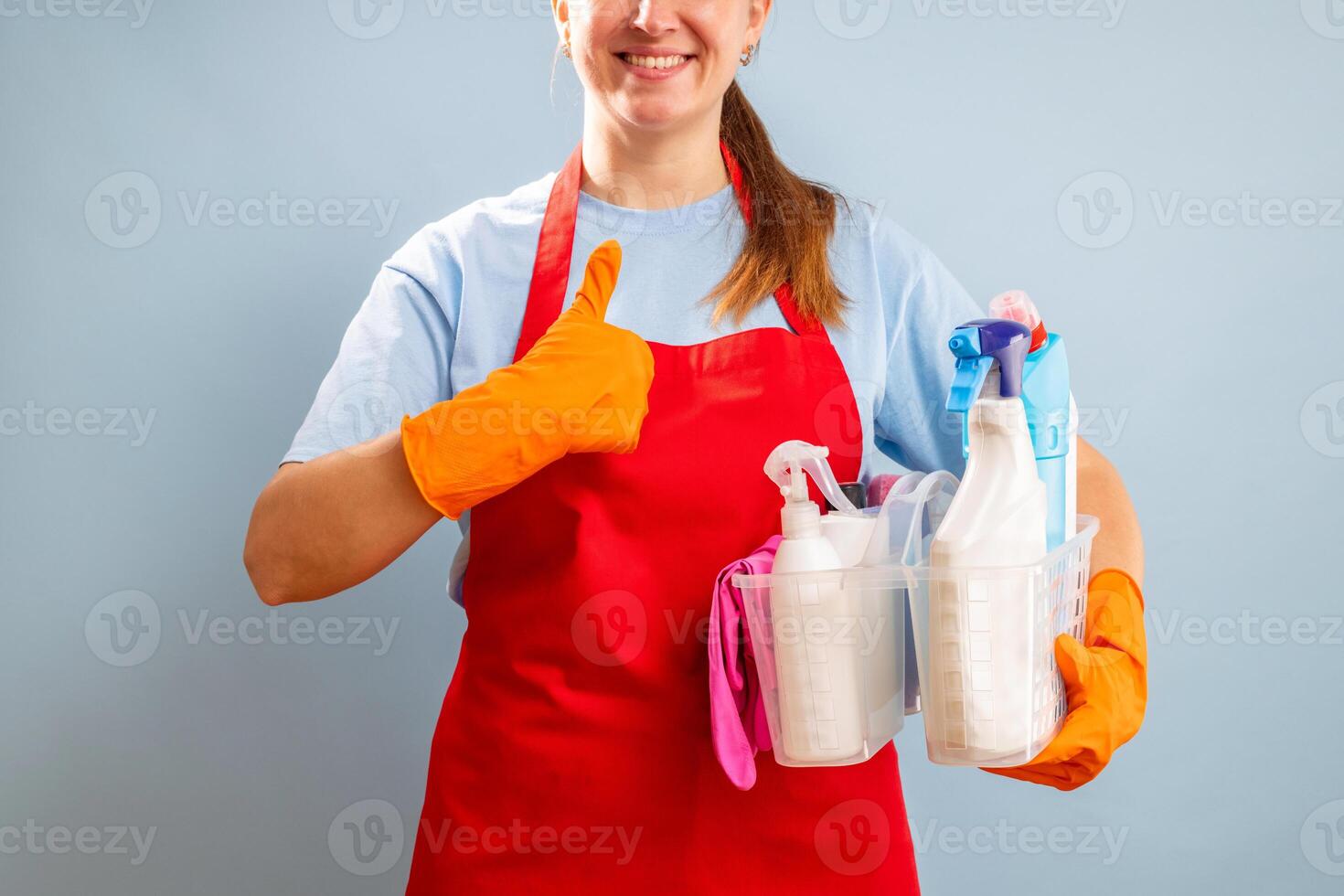Woman in gloves and apron holding basket with sponge and cleaning products photo