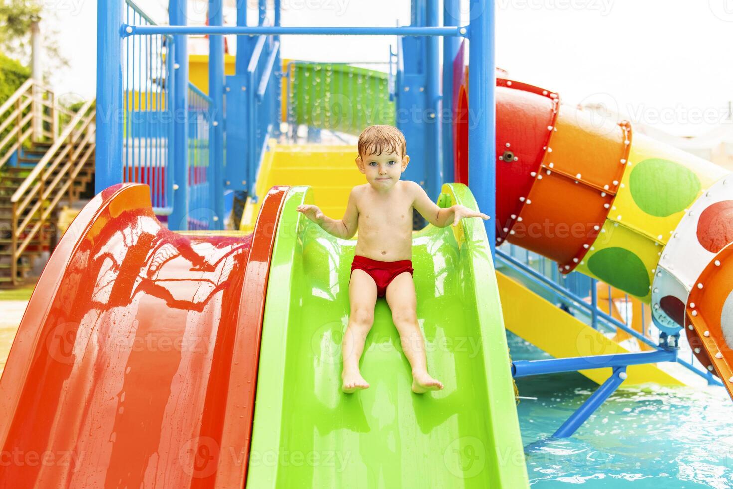 Little boy playing on water slide in outdoor pool on a hot summer day photo