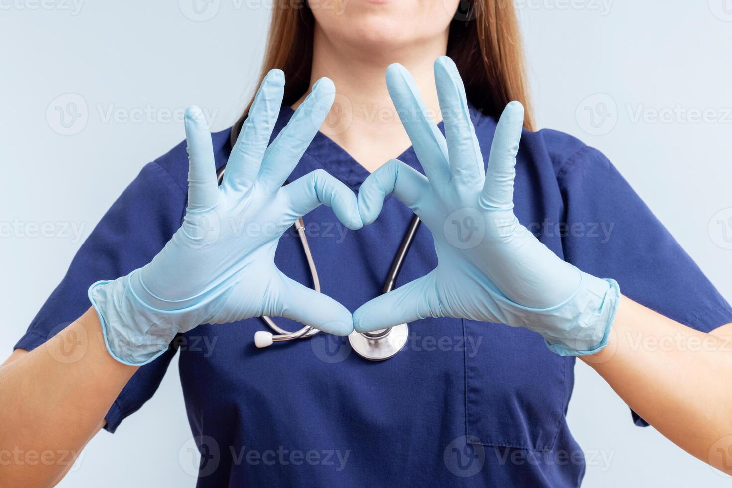 Doctor woman in gloves doing heart symbol shape with hands on blue background photo