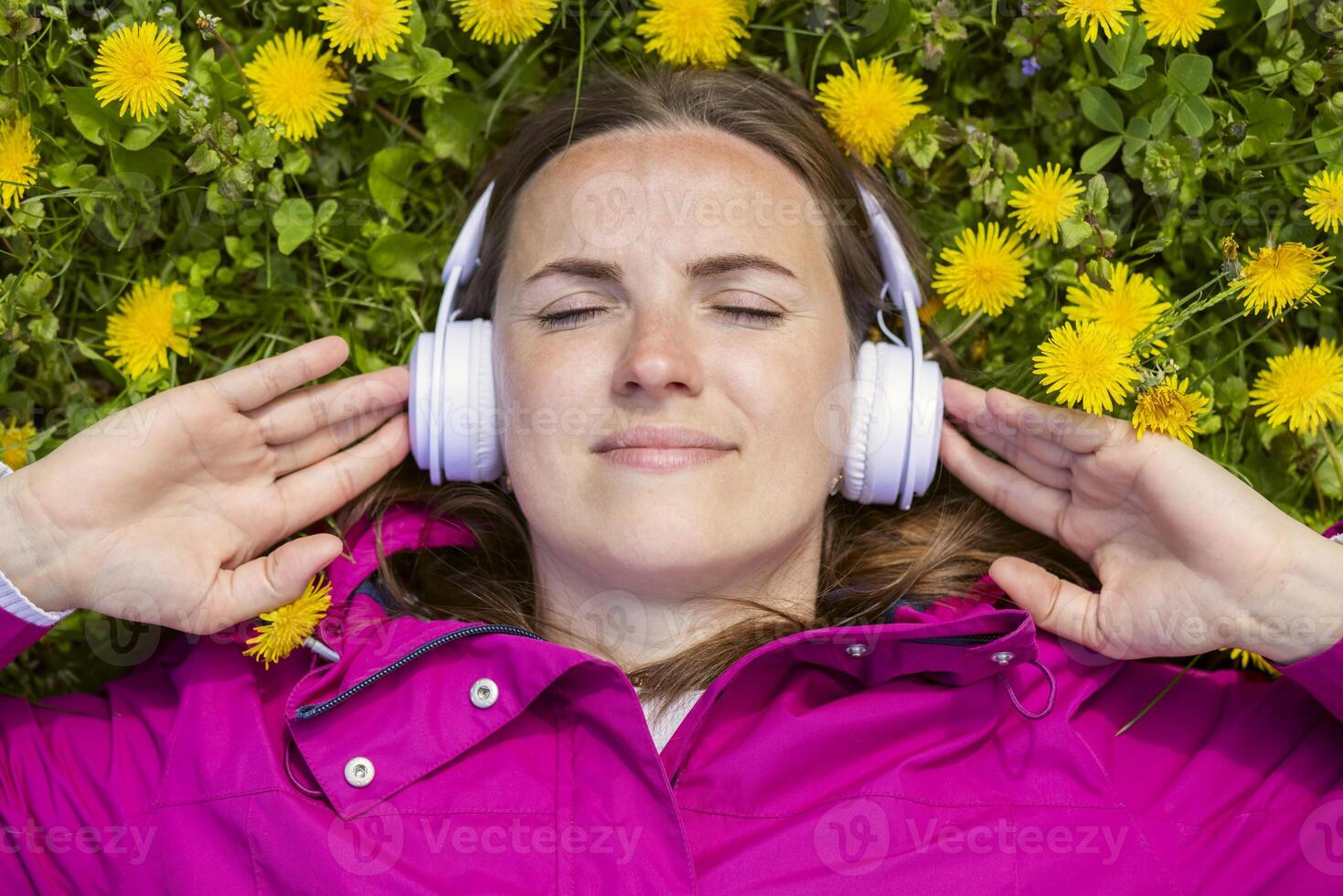Beautiful young woman in headphones listens to music lying on the grass photo