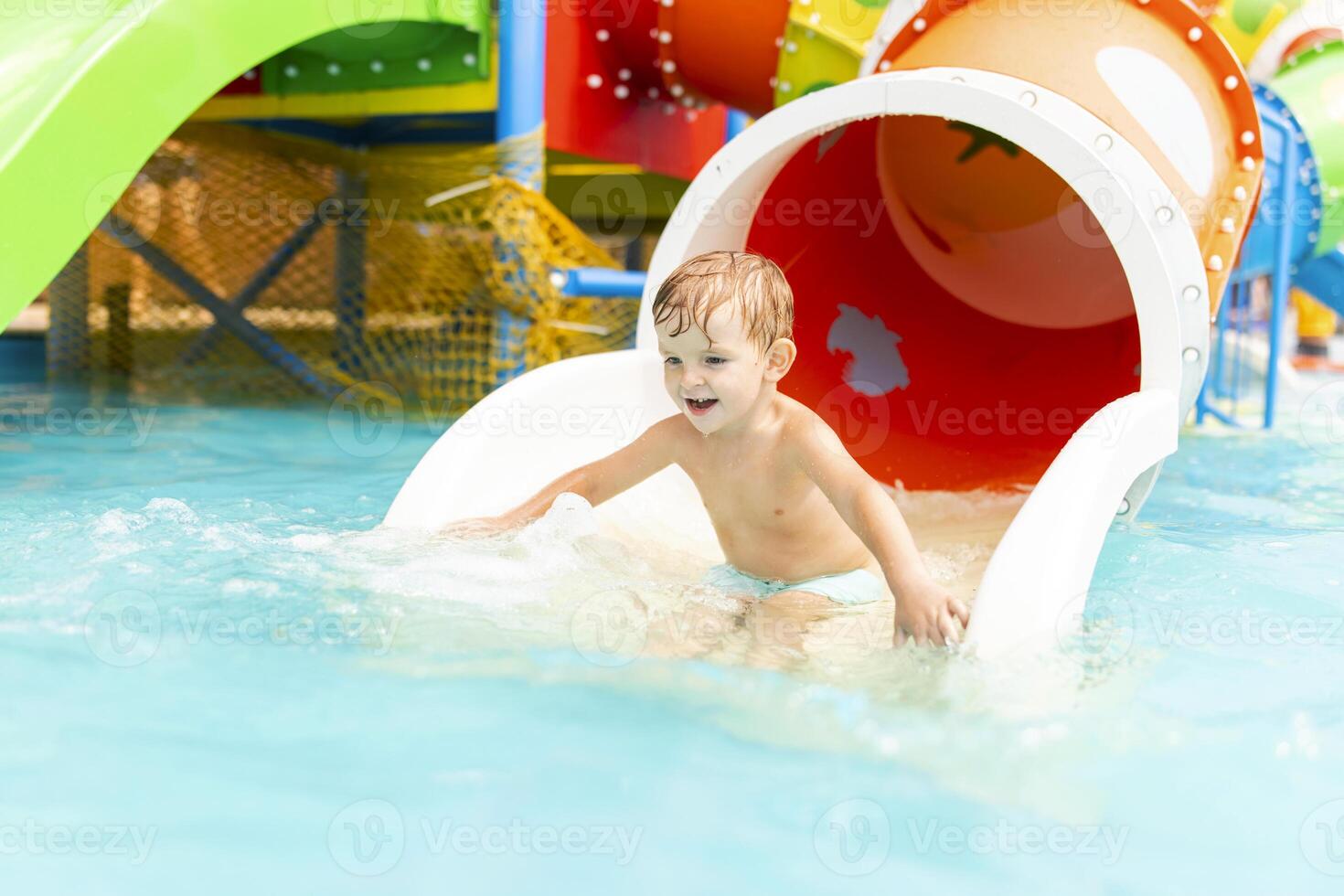 Little boy playing on water slide in outdoor pool on a hot summer day photo
