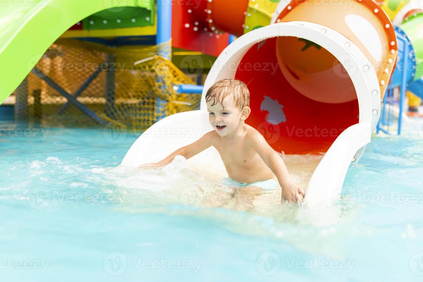 pequeño chico jugando en agua diapositiva en al aire libre piscina en un caliente verano día foto