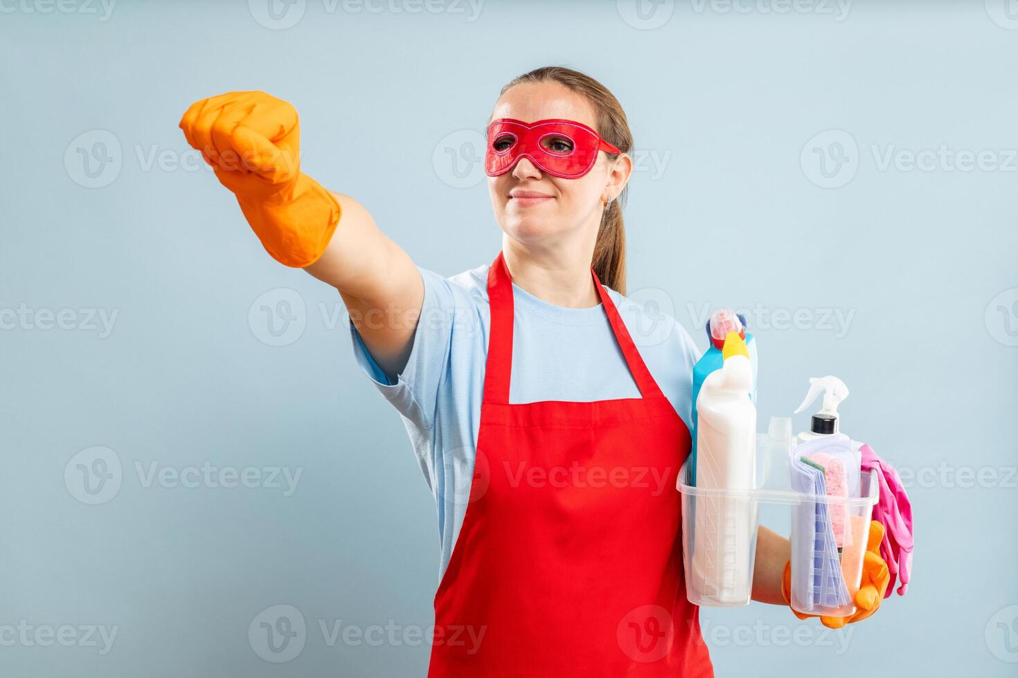 Woman in red mask, gloves and apron holding basket with cleaning supplies photo