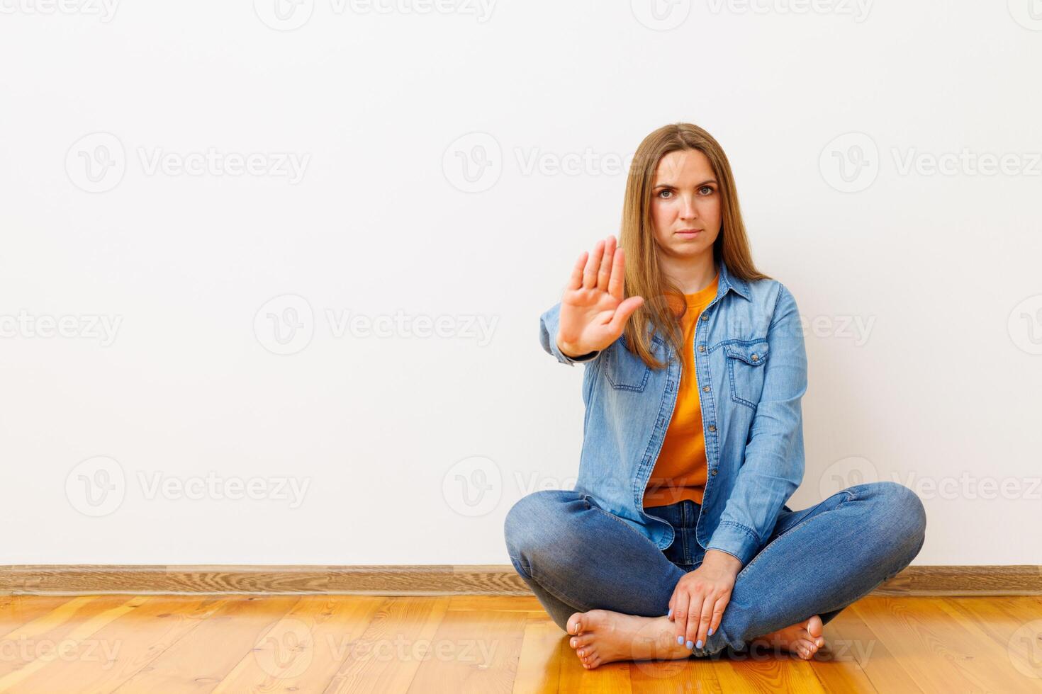 Woman in denim sitting on wooden floor showing stop gesture photo