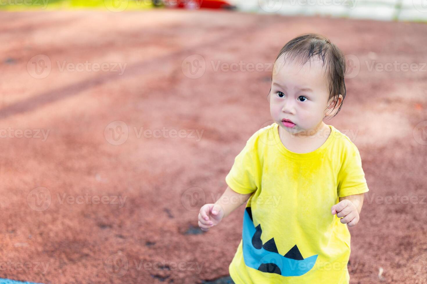 Portrait of cute Asian baby boy is walking at the playground, child looks at something, and is showing a curious face, children feels hot and sweats on body, in summer or spring, one year old toddler. photo