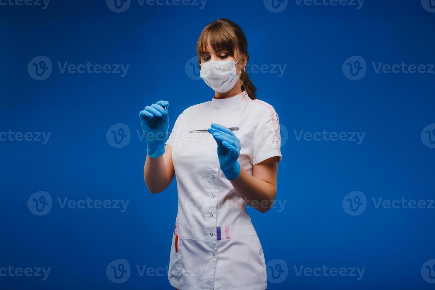 An attractive young female doctor holds a scalpel and looks directly at the camera. Concept of healthcare, treatment and surgery. Portrait of a medical practitioner on a blue background photo