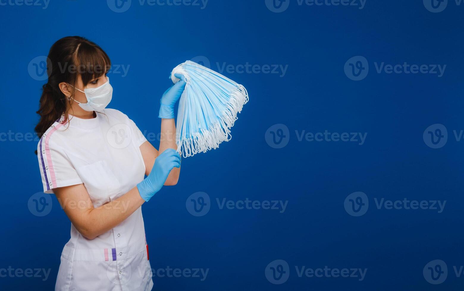 a doctor girl in a medical mask on a blue background holds a lot of protective masks in her hands photo