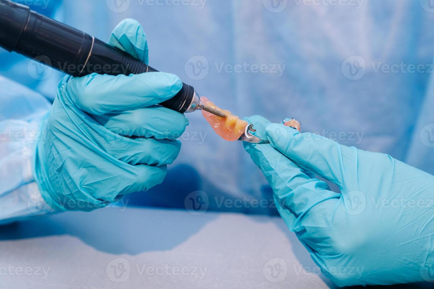 A masked and gloved dental technician works on a prosthetic tooth in his lab photo