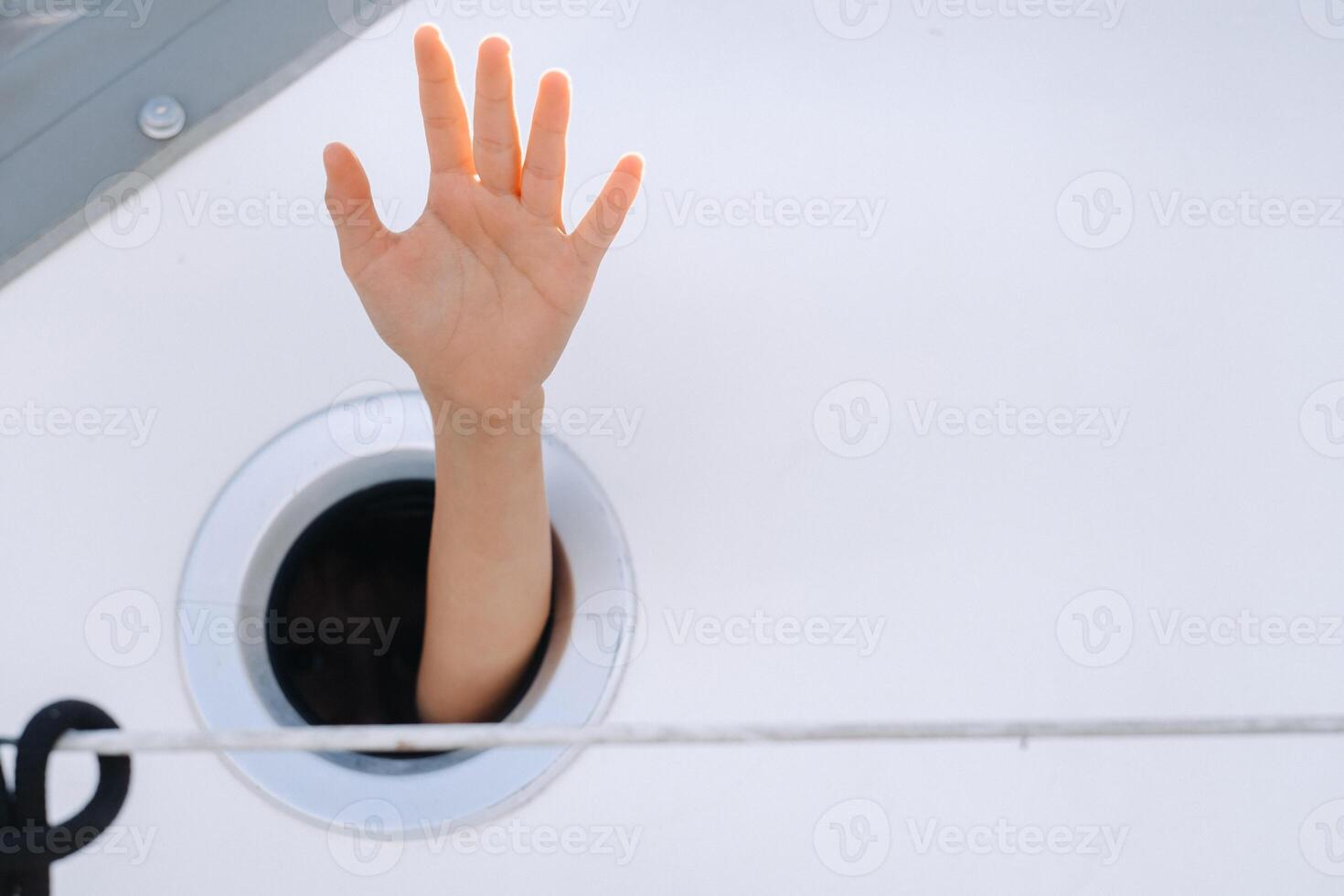 A man's hand sticks out of the porthole window on a ship at sea photo