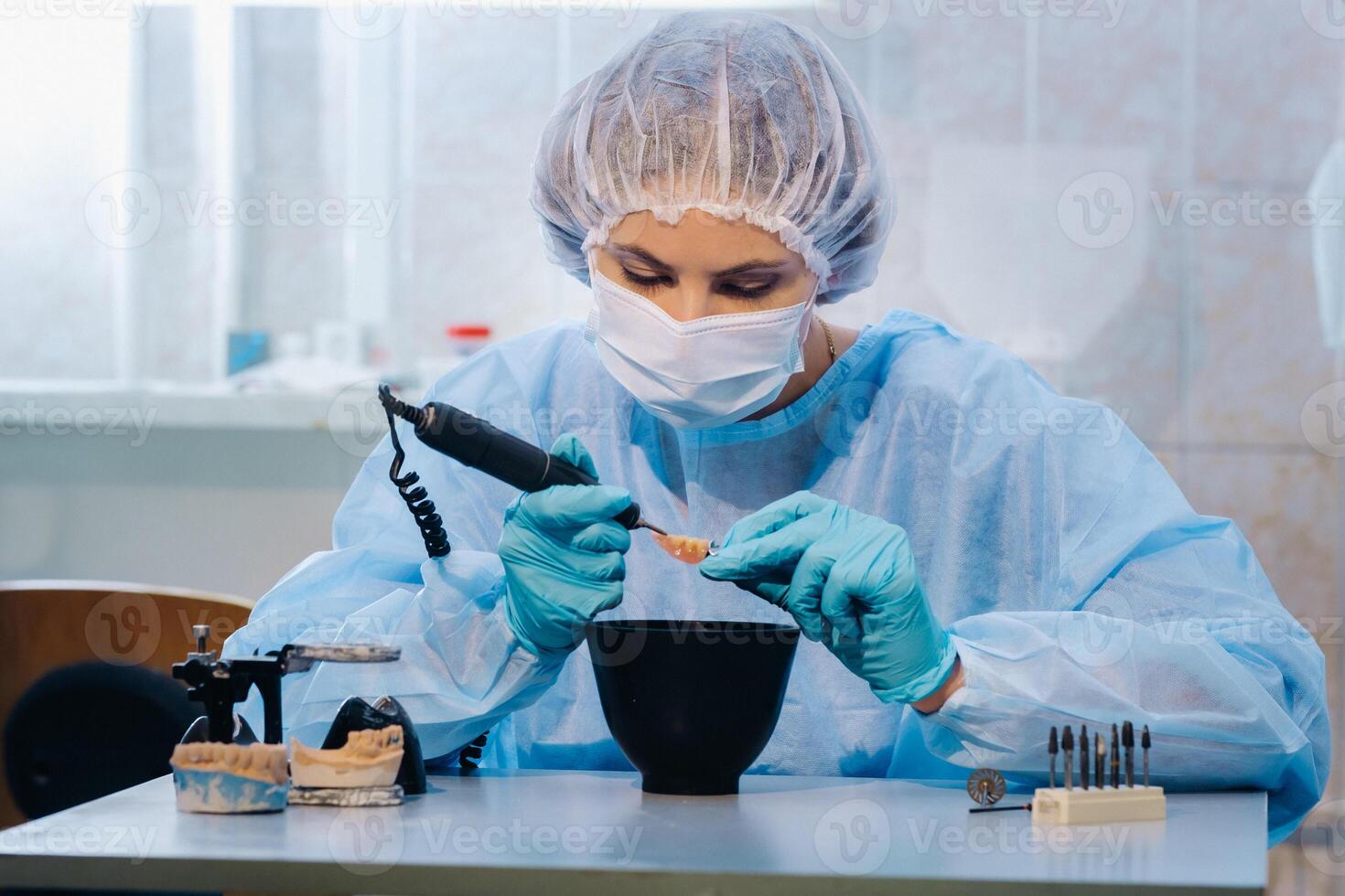 A dental technician in protective clothing is working on a prosthetic tooth in his laboratory photo