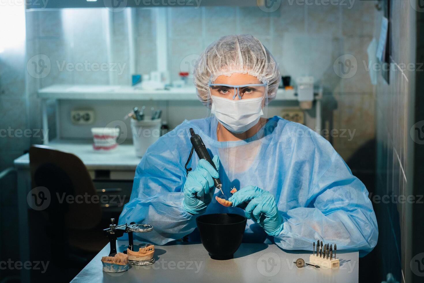 A masked and gloved dental technician works on a prosthetic tooth in his lab photo