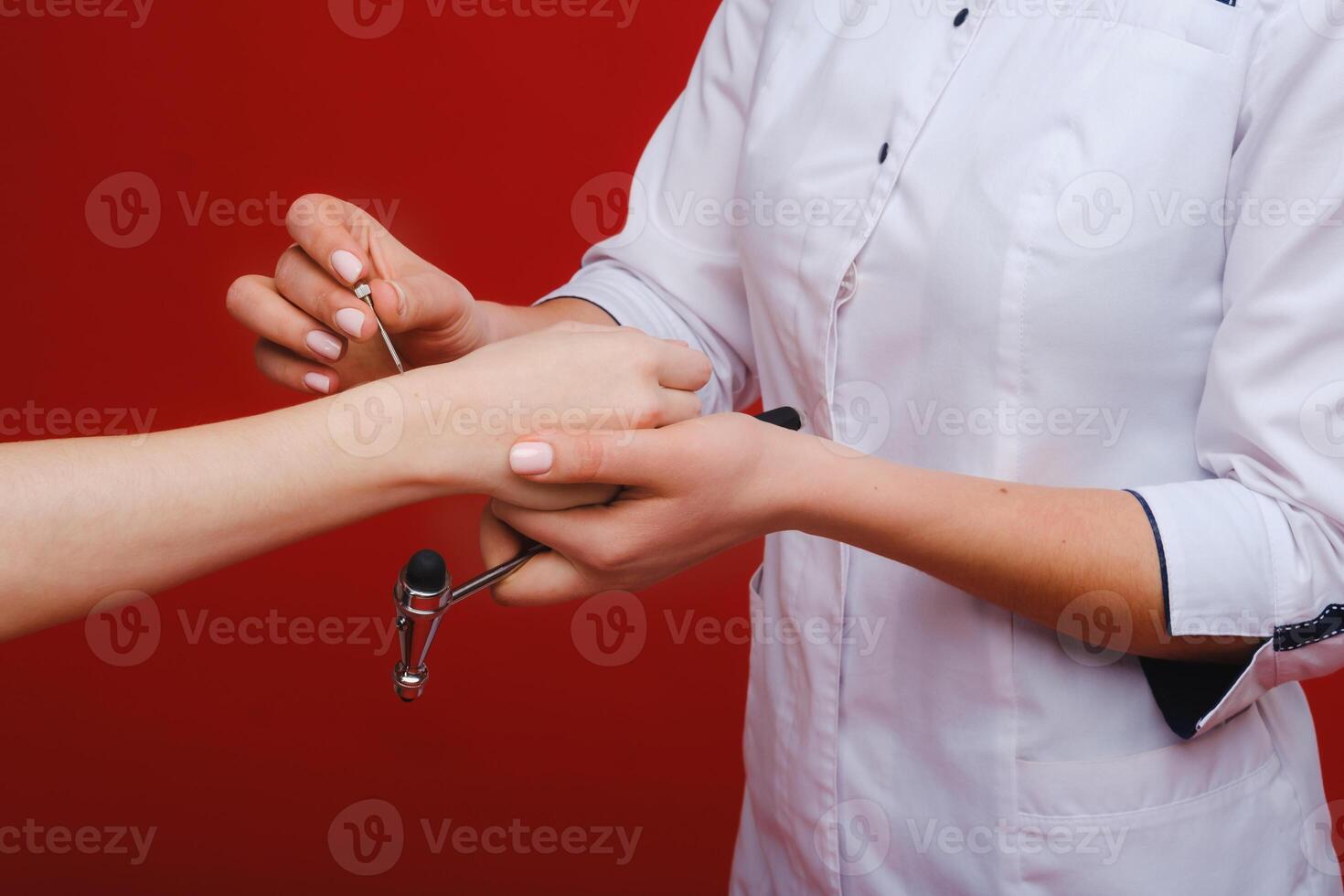 The doctor is holding a neurological hammer on a red background. The neurologist checks the patient's reflexes with a hammer. Diagnostics, healthcare, and medical care photo