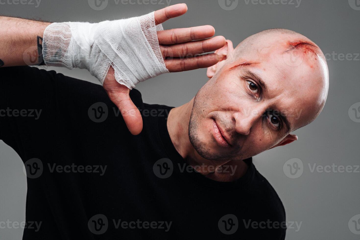 On a gray background stands a battered man in a black T-shirt With his hands wrapped up photo