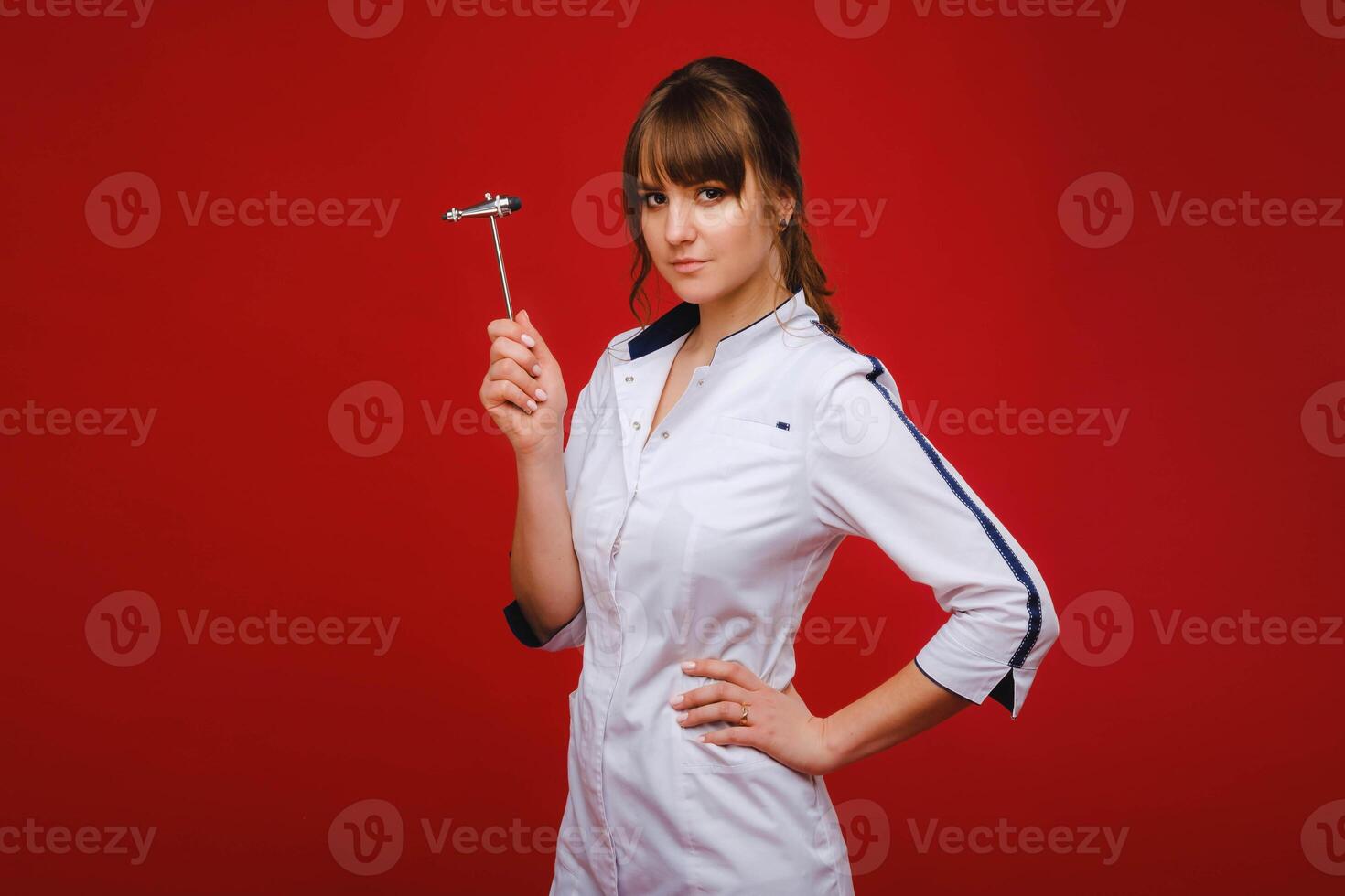 The doctor is holding a neurological hammer on a red background. The neurologist checks the patient's reflexes with a hammer. Diagnostics, healthcare, and medical care photo