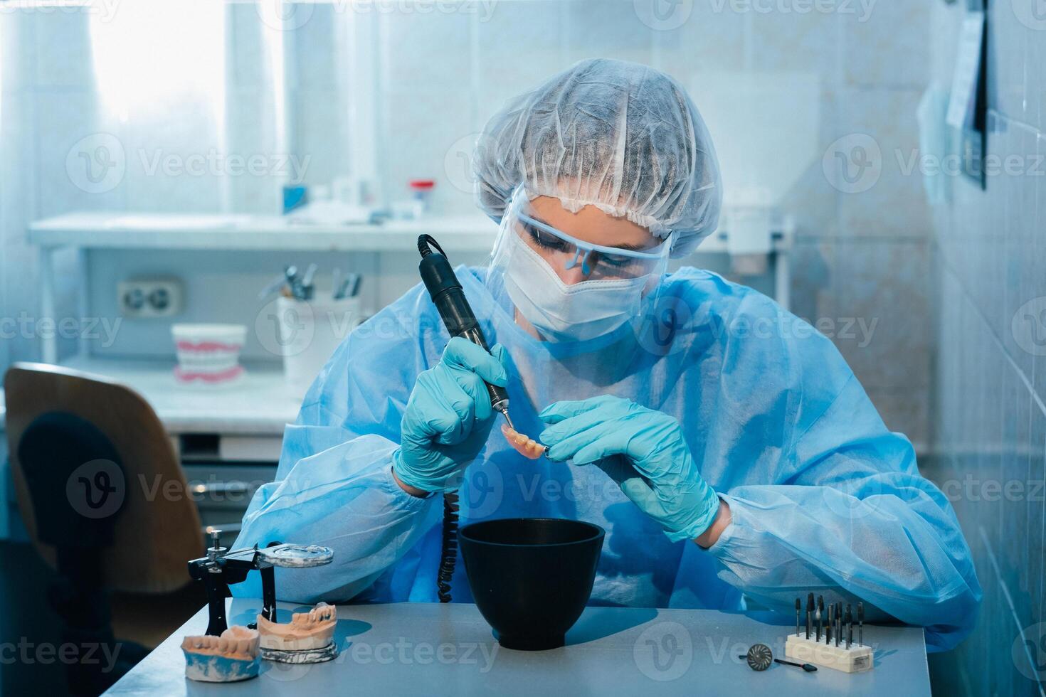 A masked and gloved dental technician works on a prosthetic tooth in his lab photo