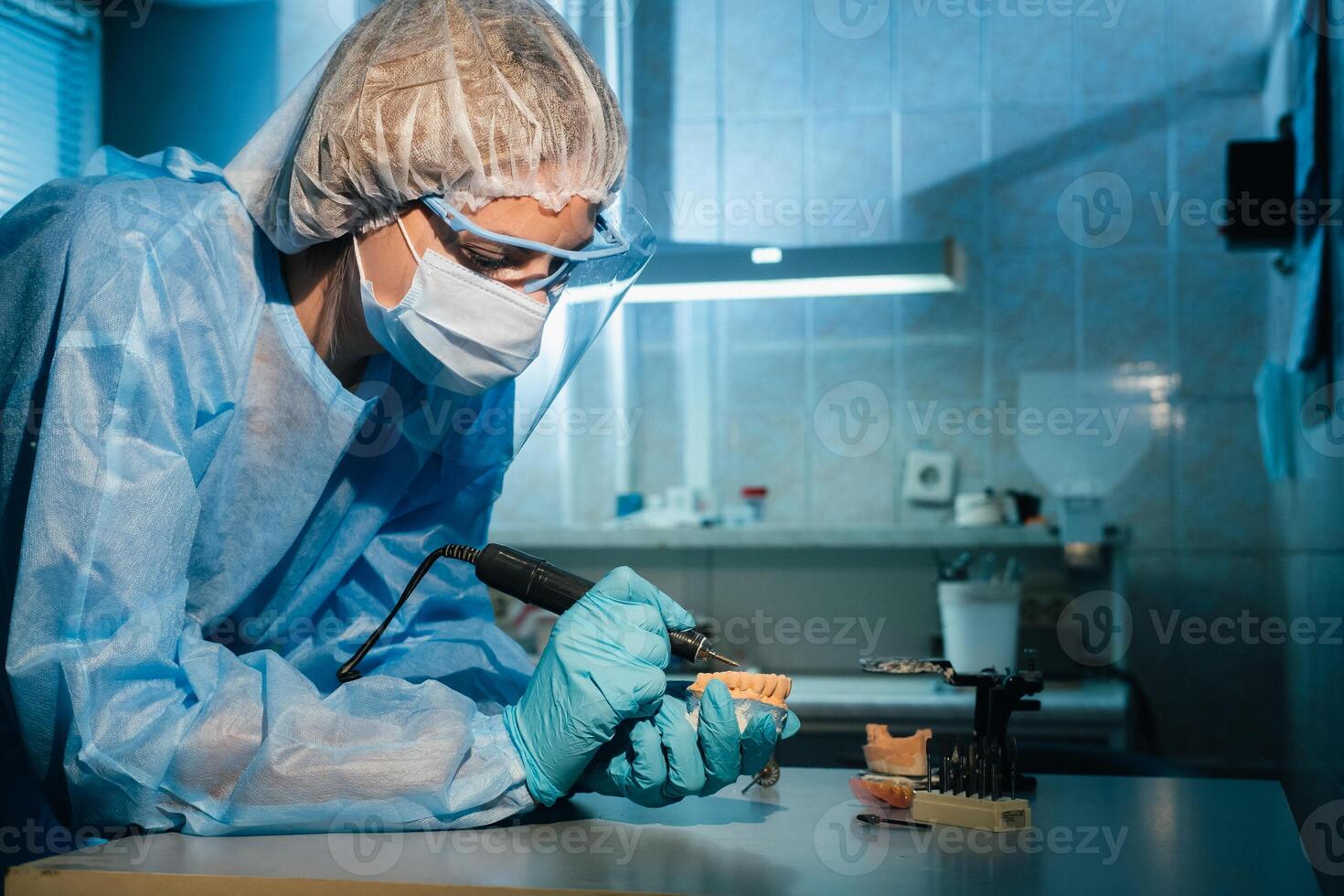 A masked and gloved dental technician works on a prosthetic tooth in his lab photo