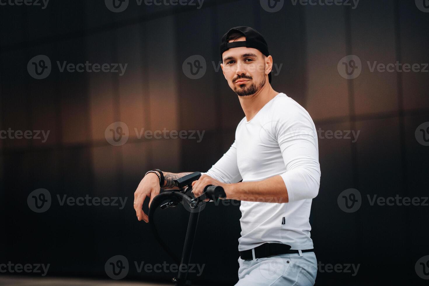 stylish guy in a white t-shirt and cap on an electric scooter in the city photo