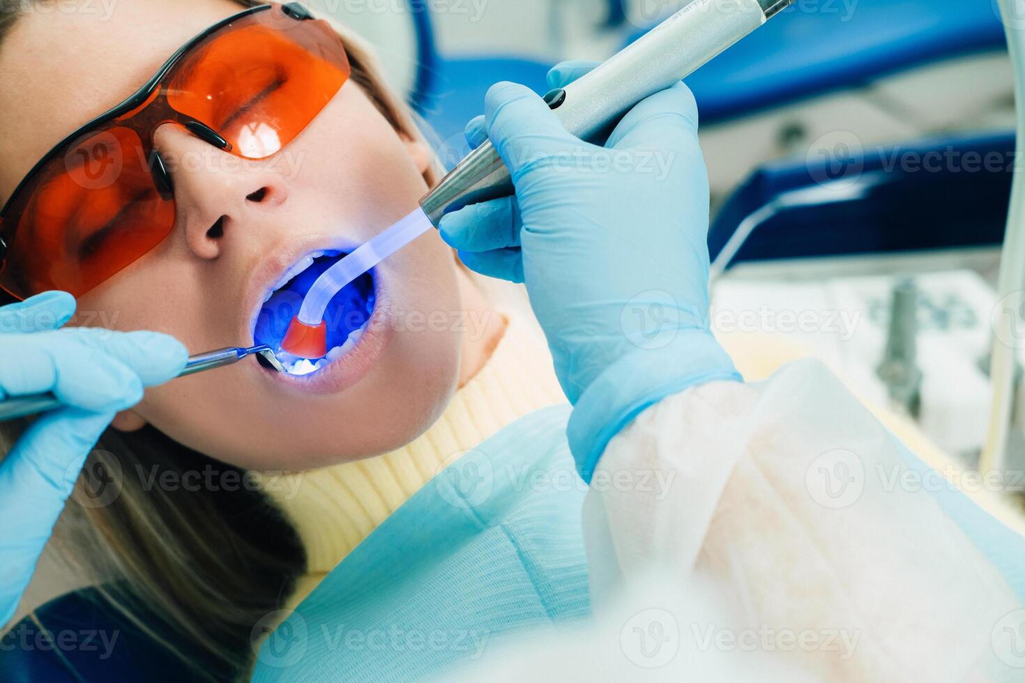 A young beautiful girl in dental glasses treats her teeth at the dentist with ultraviolet light. filling of teeth photo